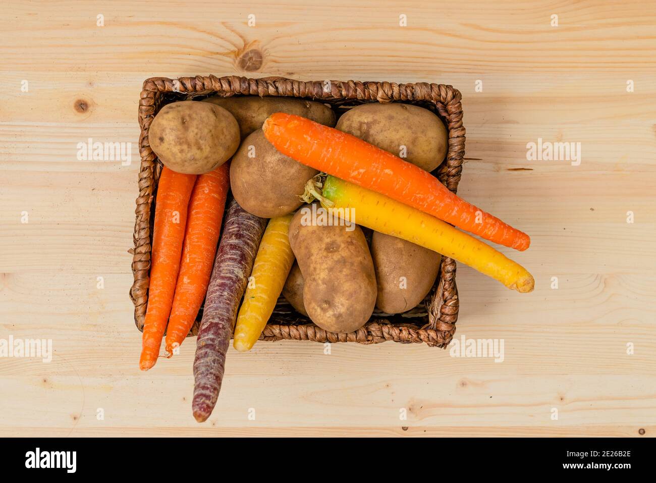 Bio-Karotte in vielen Farben und Kartoffeln in Nahaufnahme Ein Korb auf Holz rustikalen Hintergrund direkt von oben Stockfoto