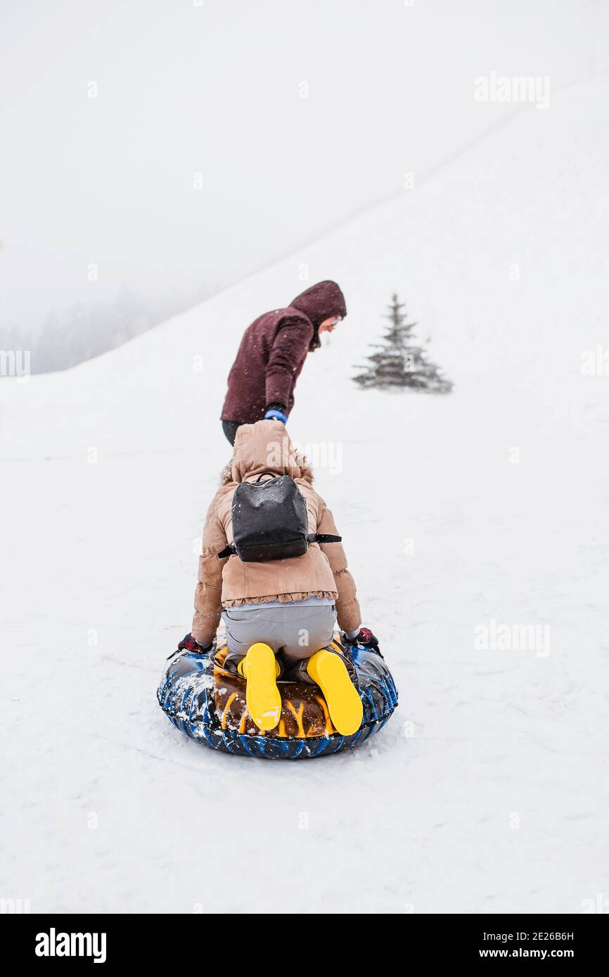 Ein Mann rollt eine Frau auf einem Schlauch für ein Seil durch den Schnee in den Bergen - eine starke blizzard auf der Skipiste - Bewegungsunschärfe Stockfoto