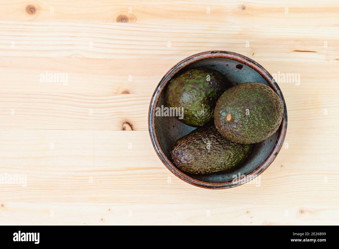 Drei reife Bio-Avocado in einer Schale, flach liegend, heller Holzhintergrund mit Kopierraum Stockfoto