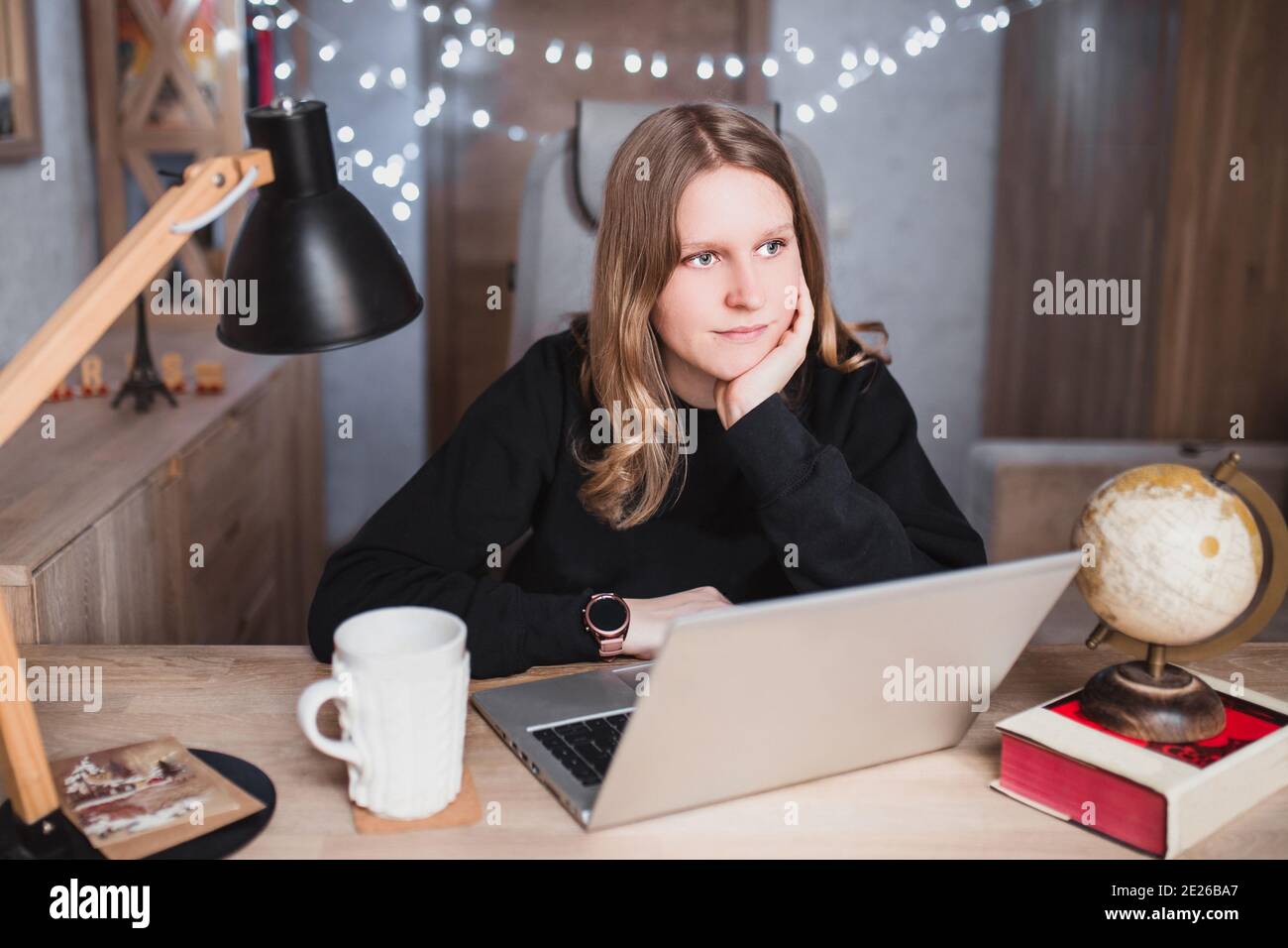 Junge blonde Frau zu Hause in einem gemütlichen Zimmer Der Tisch lehnte ihre Ellbogen und dachte an den Computer Blick in die Ferne Stockfoto