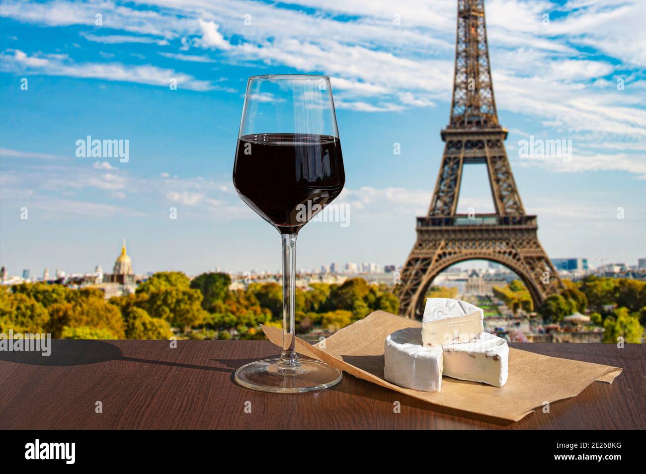Ein Glas Wein mit Brie-Käse auf dem Eiffelturm und im Hintergrund der Skyline von Paris. Sonniger Blick auf ein Glas Rotwein mit Blick auf den Eiffelturm in Paris Stockfoto