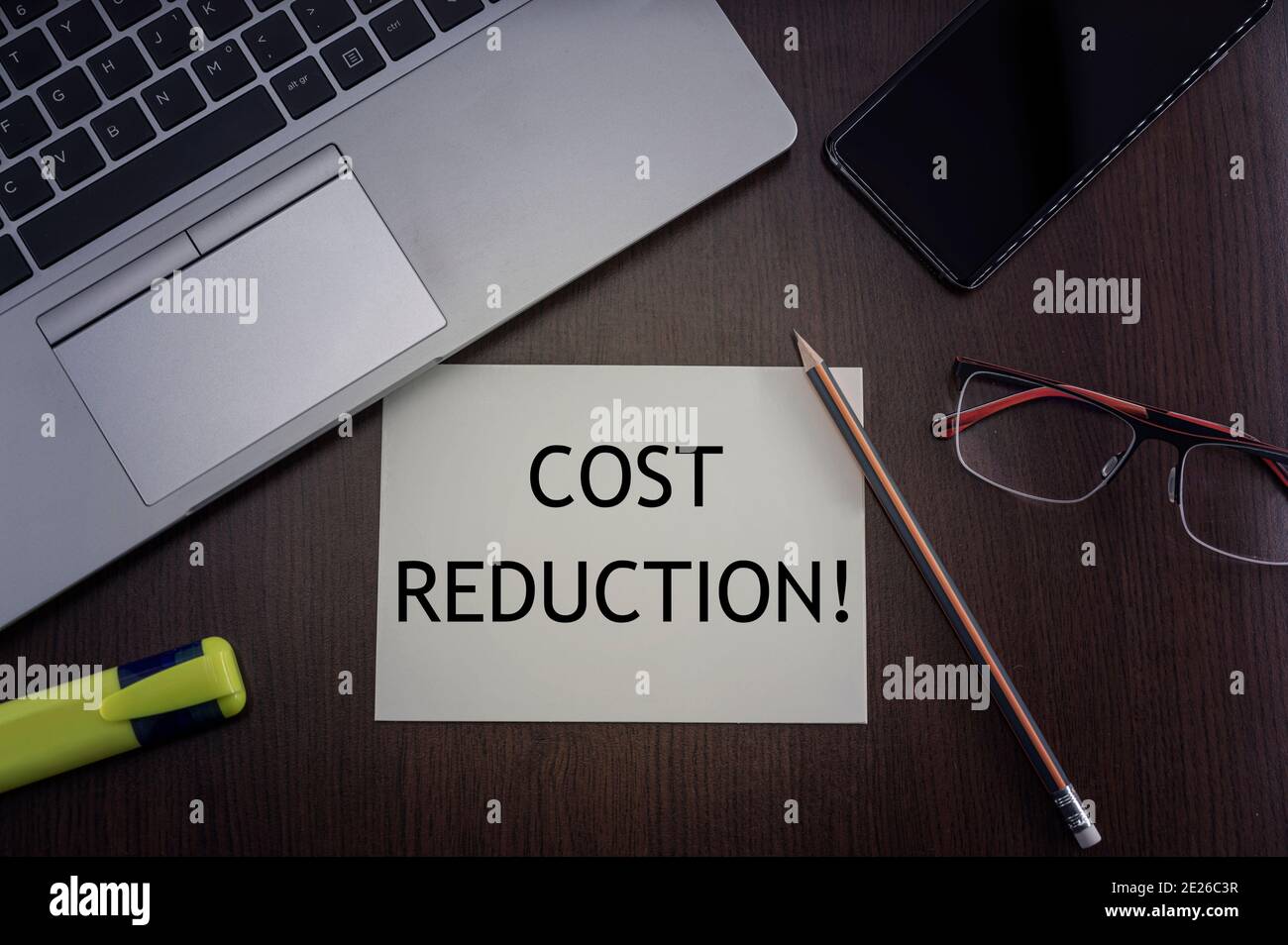 Draufsicht auf Laptop, Telefon, Brille und Bleistift mit Karte mit Aufschrift Kostenreduzierung. Stockfoto