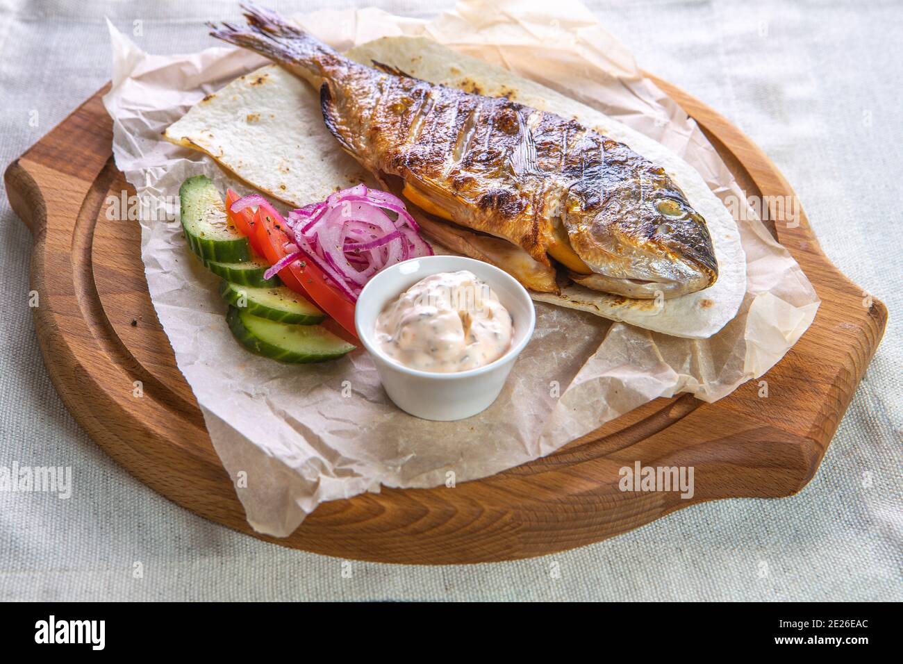 Gegrillter dorado-Fisch mit Sauce, Gurken, Tomaten und Zwiebeln auf einem Holztablett Stockfoto