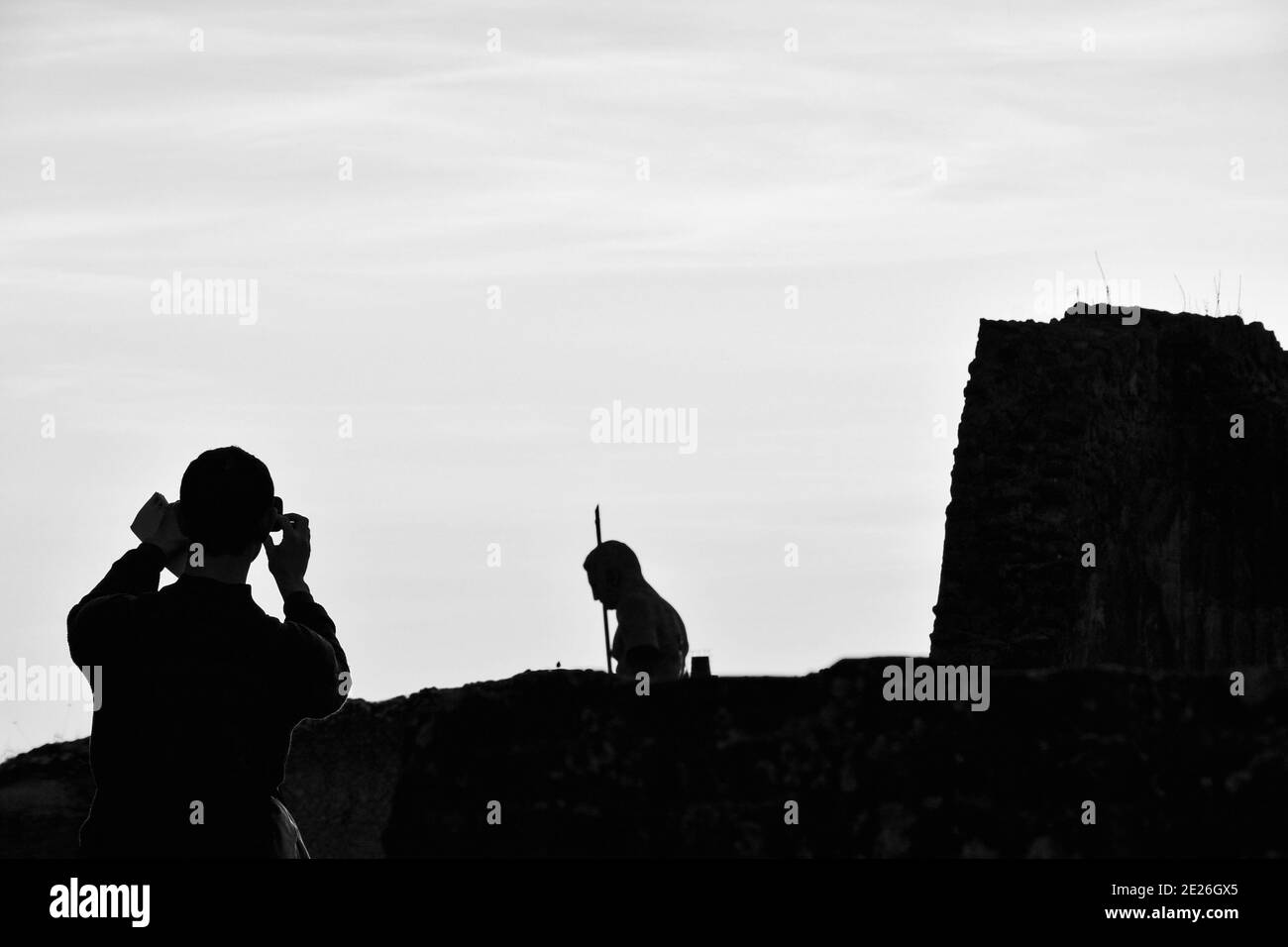 Ruinen von Pompeji. Junge Tourist mit Karte in der Hand Foto mit Smartphone von Pompeji Ruinen mit zerstörten Wand und Krieger Statue. Schwarzweißfoto. Stockfoto