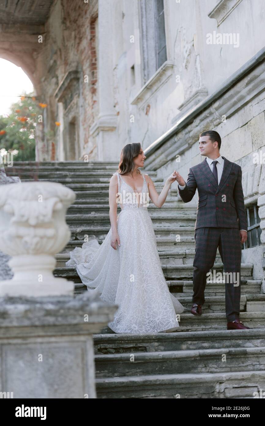 Braut und Bräutigam, die im alten Palast über eine Treppe hinuntergehen und sich gegenseitig angucken. Hochzeitspaar. Hochzeitsfoto Stockfoto