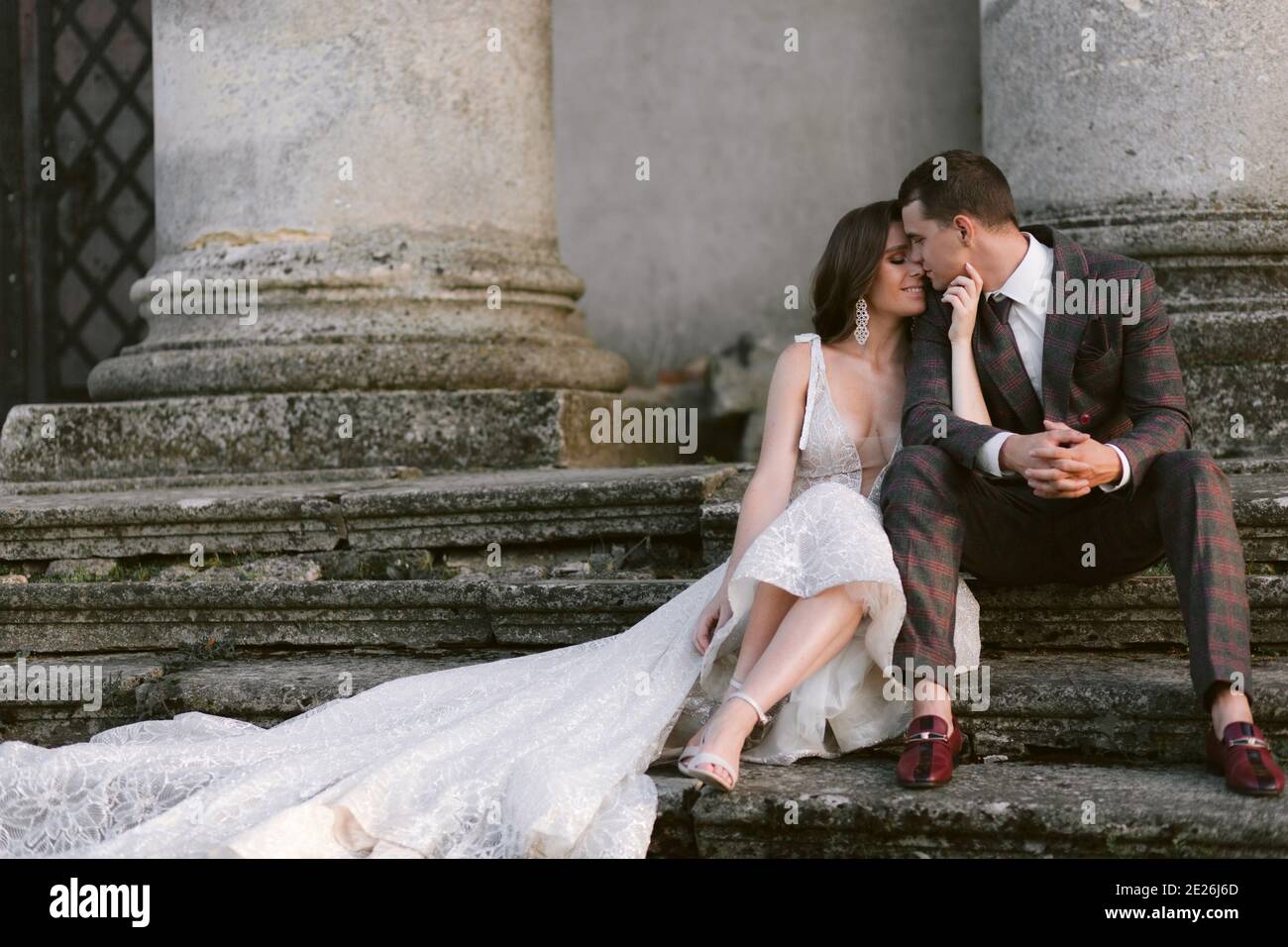 Glückliche Braut und Bräutigam sitzen auf der Treppe des alten Palastes vor den Säulen. Hochzeitspaar. Hochzeitsfoto Stockfoto