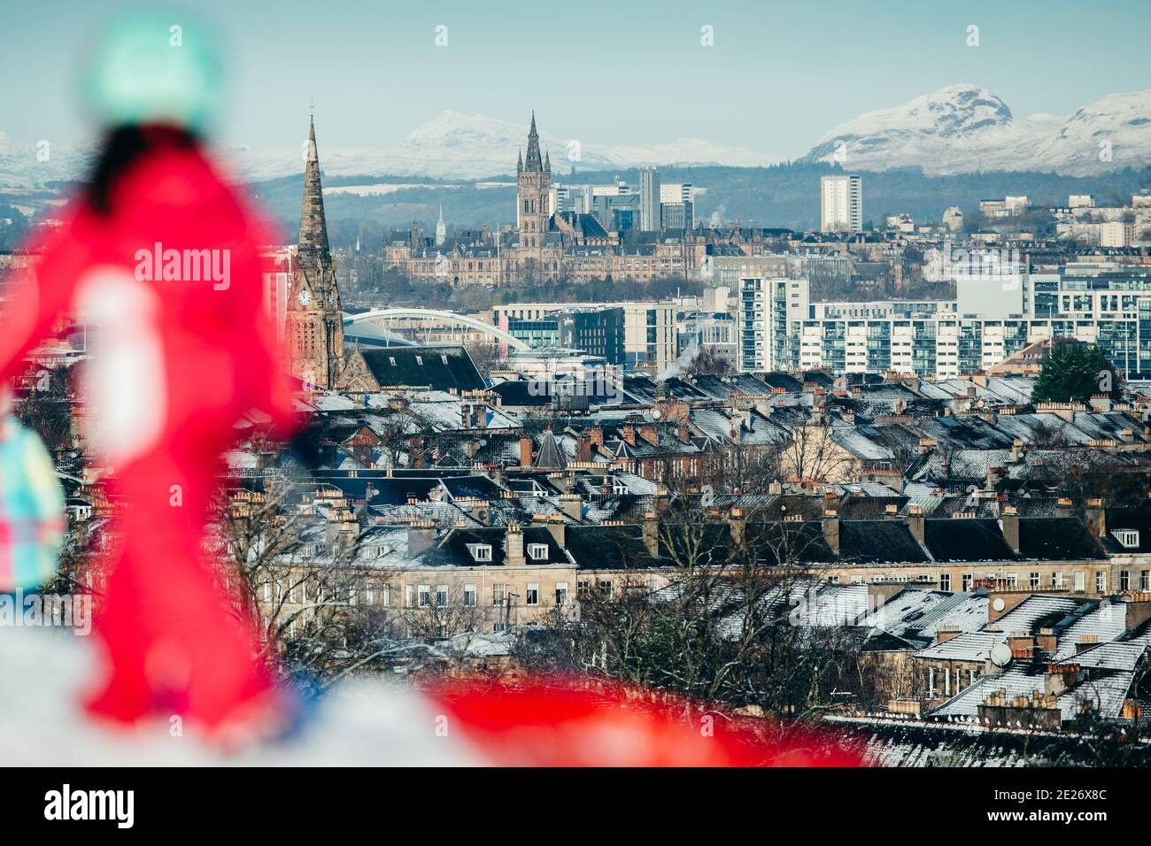 Mädchen, die mit dem Schlitten im Queens Park im Schnee spazieren, mit der Stadt Glasgow im Hintergrund. Stockfoto