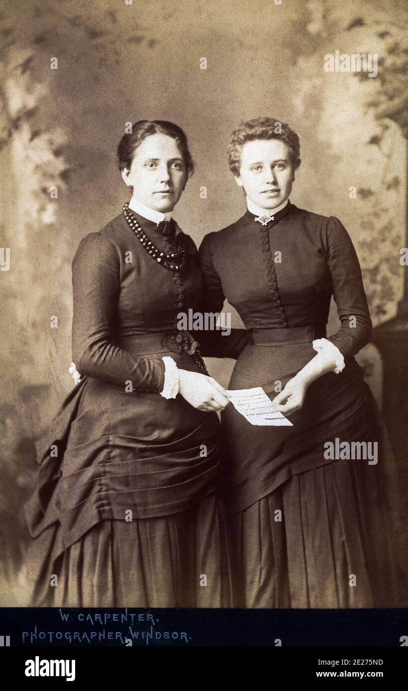 Zwei modisch gekleidete viktorianische Frauen aus den 1880er Jahren, möglicherweise Schwestern, freuen sich, einen Brief erhalten zu haben. Stockfoto