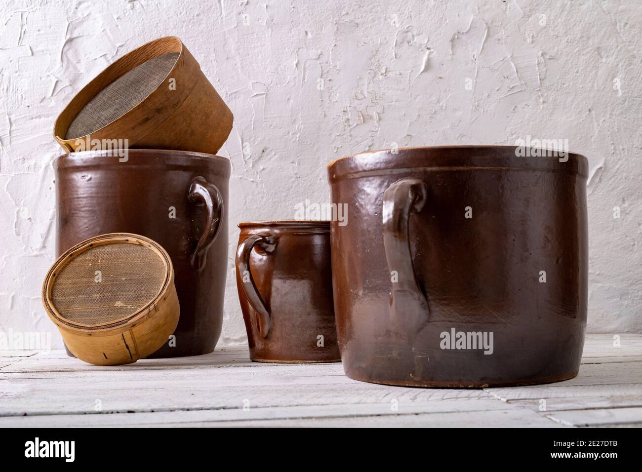 Ein Tontopf und ein Holzsieb auf weißem Wandhintergrund. Alte Accessoires im Haushalt. Heller Hintergrund. Stockfoto