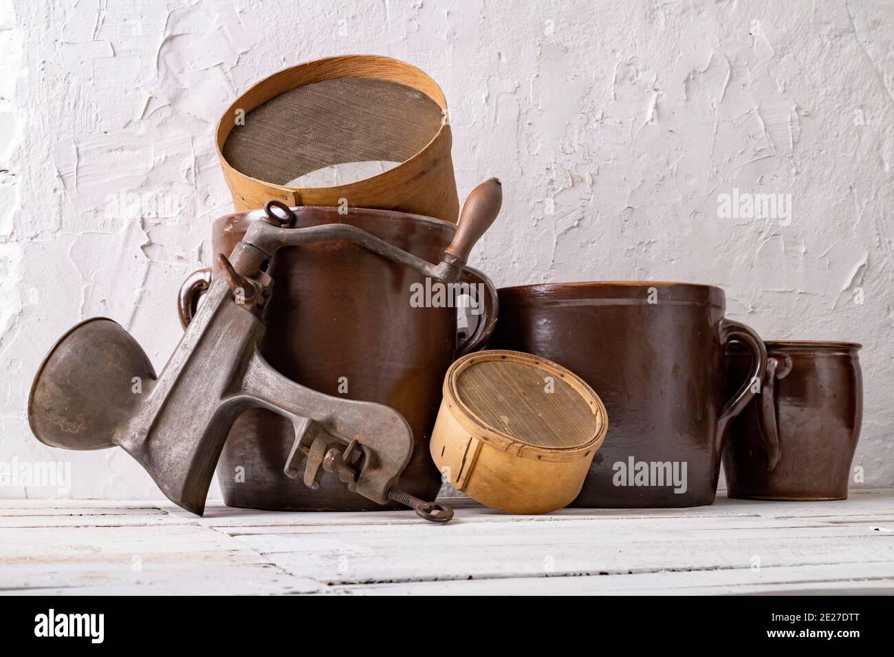 Ein Tontopf, ein Holzsieb und ein Metallgerät zum Entsaften an einer weißen Wand. Alte Accessoires im Haushalt. Heller Hintergrund. Stockfoto