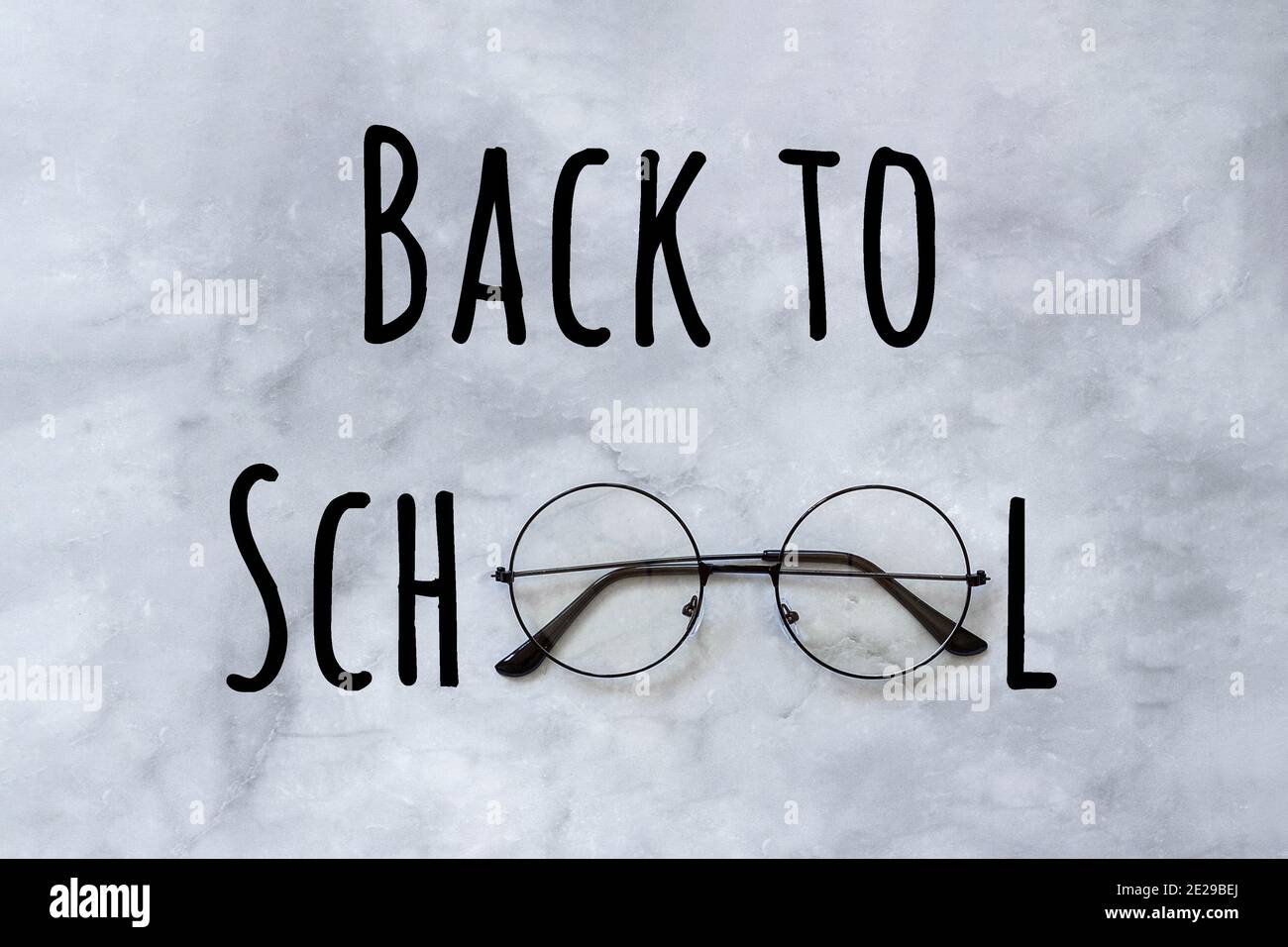 Zurück zur Schule Text und stilvolle schwarze runde Brillen Brille auf Marmor Hintergrund. Konzeptbildung. Grußkarte von oben. Stockfoto