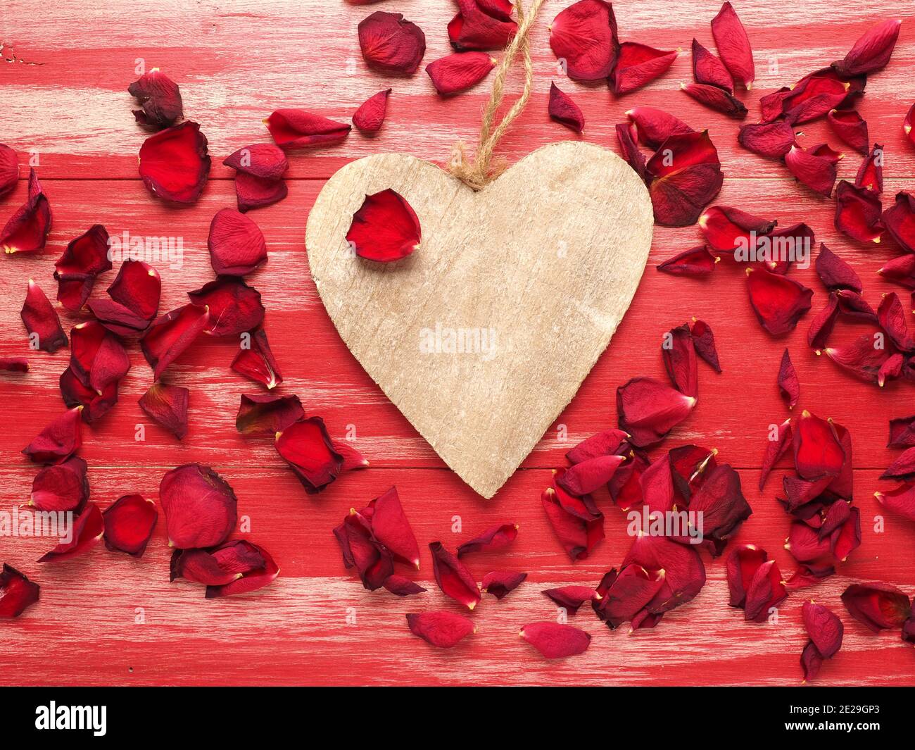 Rustikales Holzherz mit Rosenblättern auf roten Holzbohlen Stockfoto