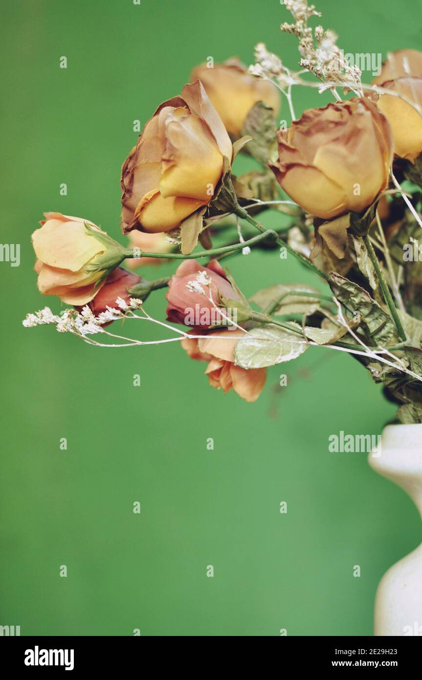 Ein Teil eines Buketts aus herbstlich braunen künstlichen Rosen auf grünem Hintergrund mit Kopierraum. Vertikal Stockfoto