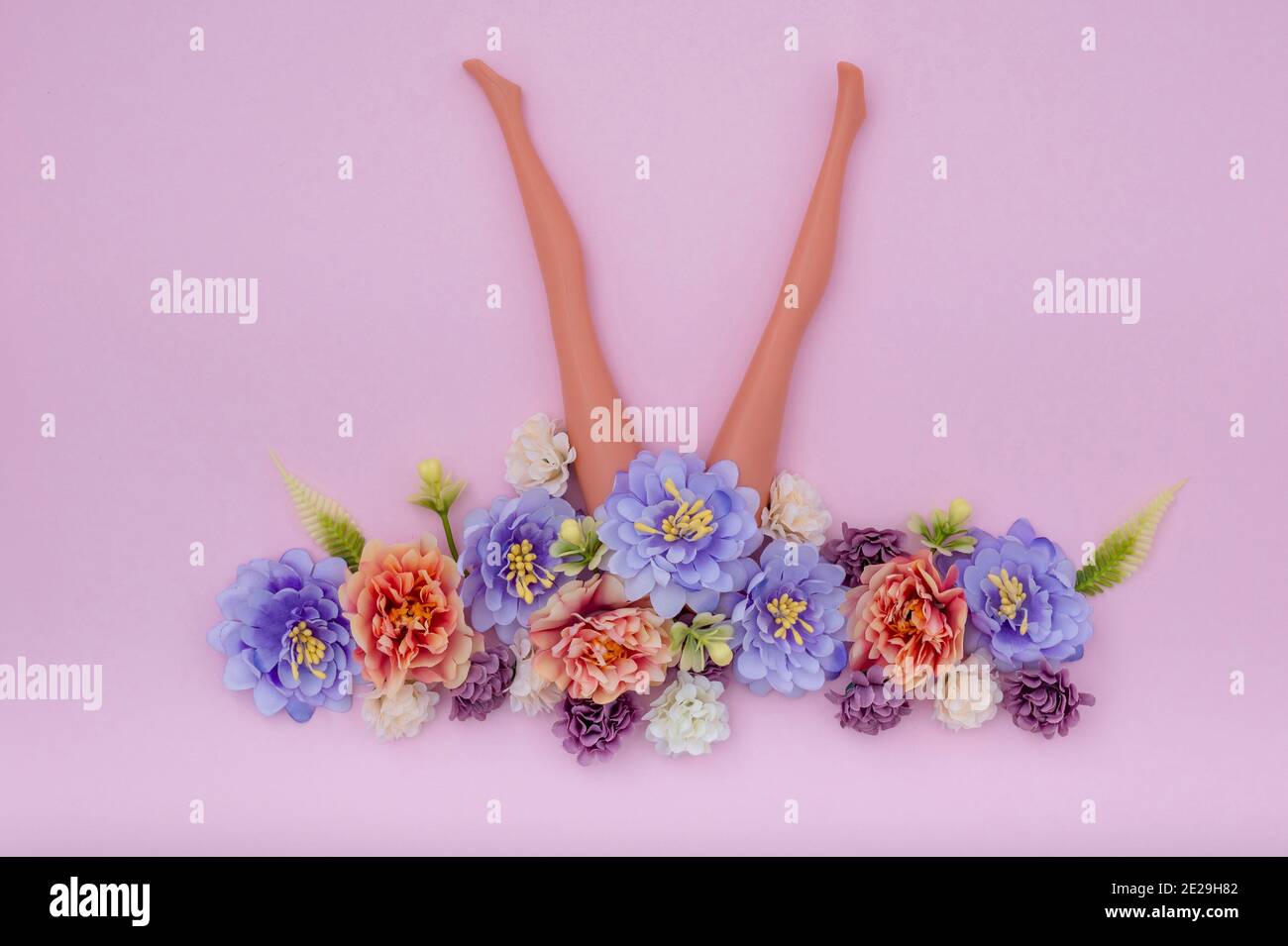Schlanke Puppenbeine mit künstlichen Blumen auf rosa Hintergrund Stockfoto