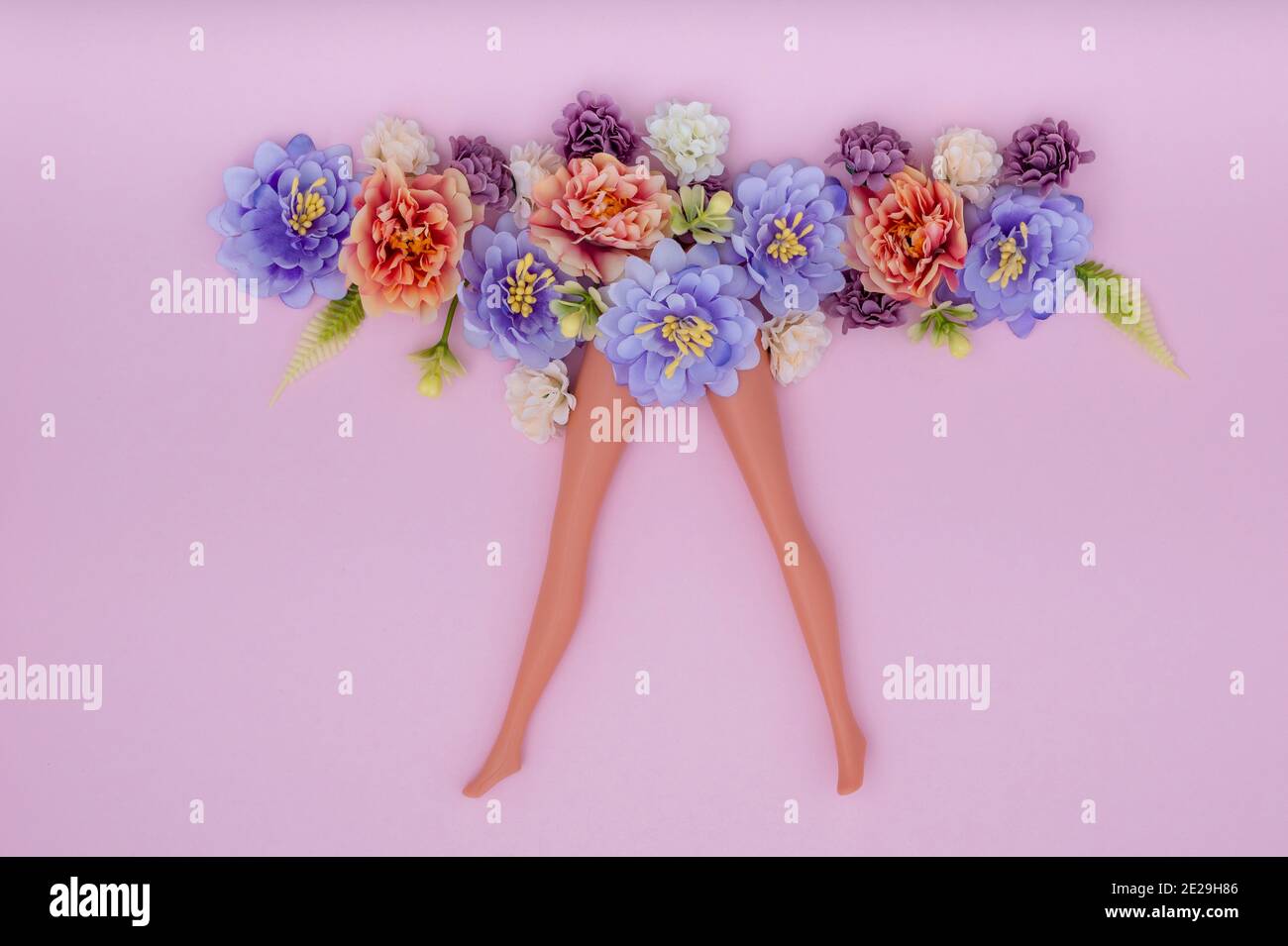 Schlanke Puppenbeine mit künstlichen Blumen auf rosa Hintergrund Stockfoto