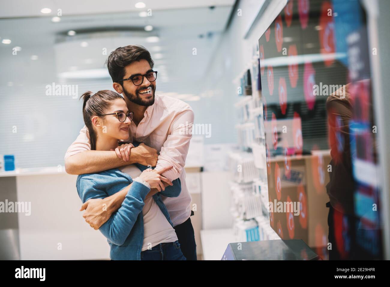 Moderne junge gerade verheiratete Paar sucht mit Zufriedenheit in ihrem neuen großen Fernsehbildschirm im Tech-Geschäft. Stockfoto