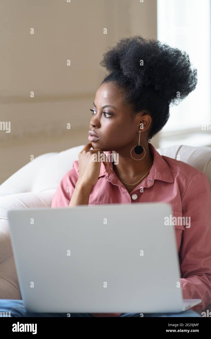 Afro American Millennial Frau mit Afro Frisur auf der Couch sitzen Pause von der Arbeit auf dem Laptop Stockfoto