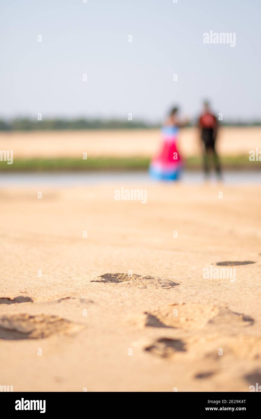 Pärchen, die an einem Strand rumhängen, verschwimmt mit Fokus Auf einem Fuß drucken auf dem Sand hinter ihnen Stockfoto