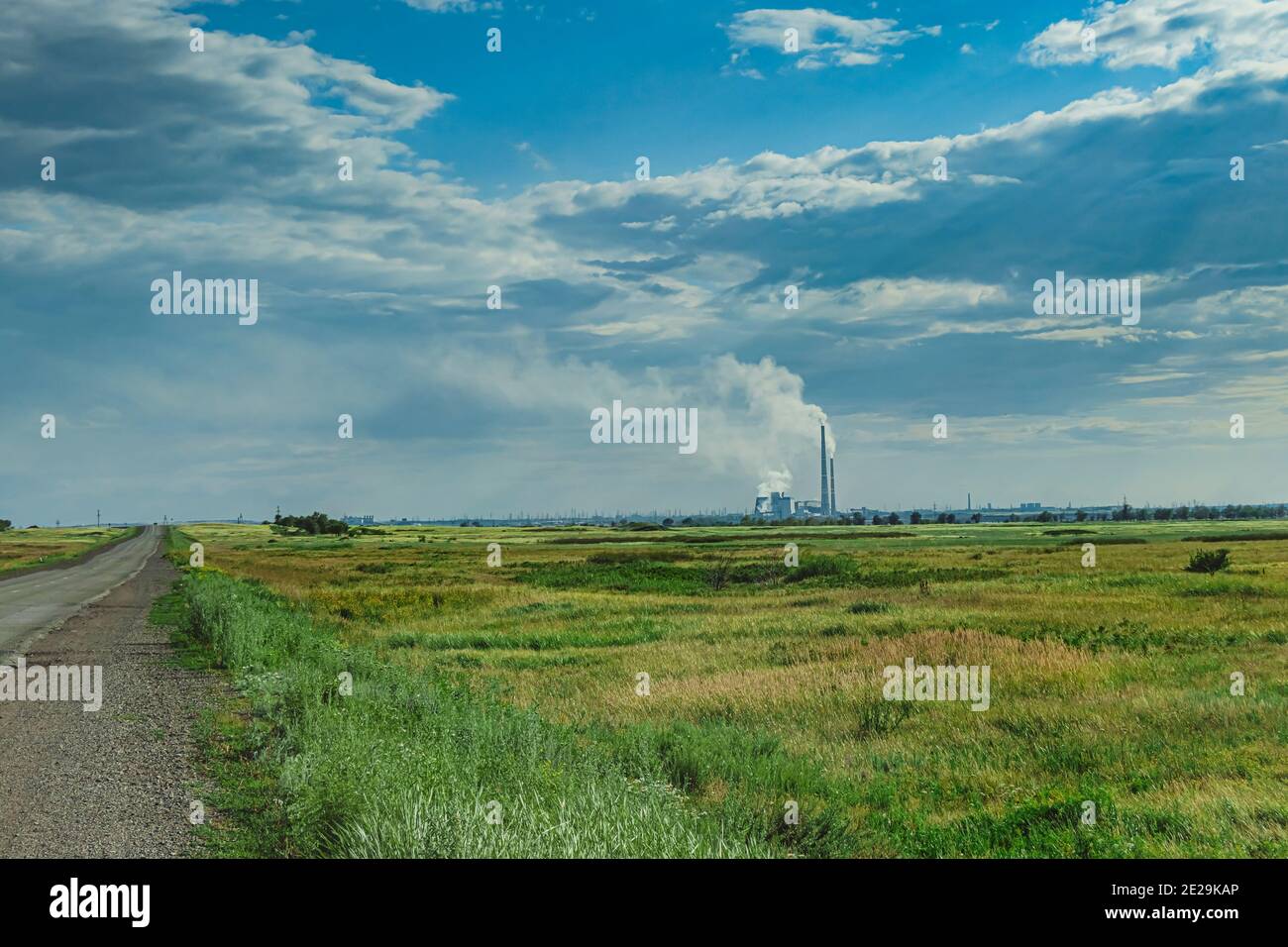 Rauchende Kamine von Pflanzen in grünem Feld auf dem Hintergrund des blauen Himmels. Konzept der Umweltverschmutzung. Menschlicher Einfluss auf die Natur. Stockfoto