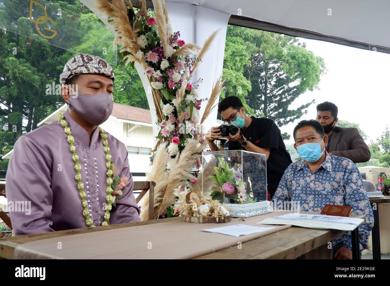 Ein Bräutigam, ein Zeuge und Fotografen mit Gesichtsmaske bei einer Hochzeitszeremonie während der Pandemie. Stockfoto