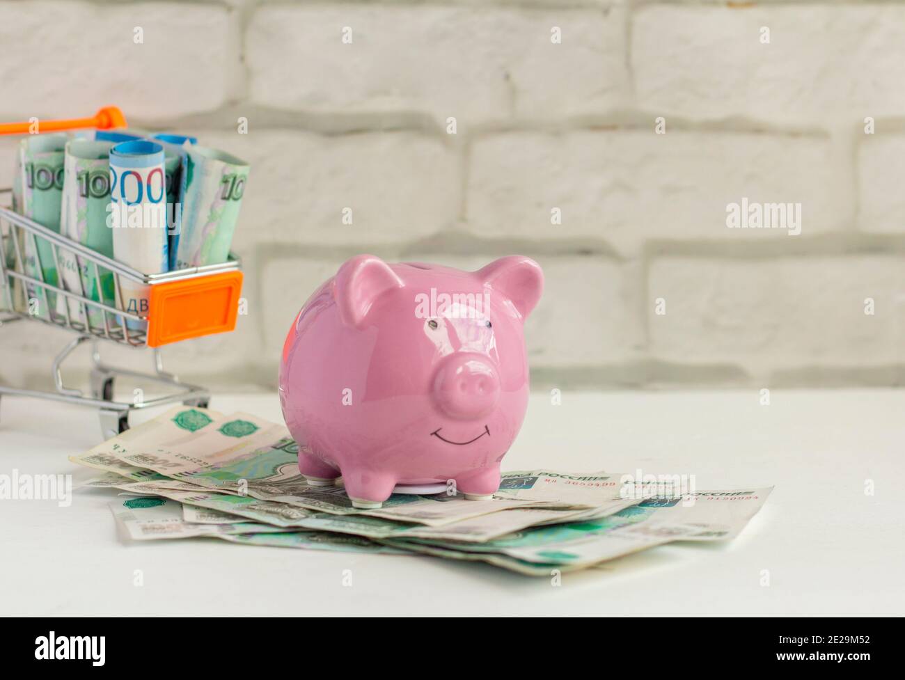 Sparschwein und Einkaufswagen mit Geld auf hellem Hintergrund. Stockfoto