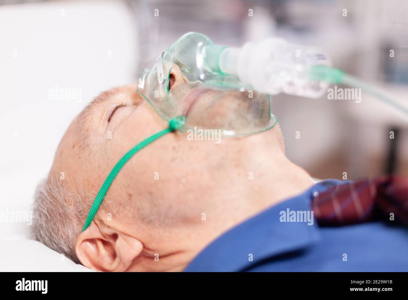 Älterer Mann beim Einatmen durch Sauerstoffmaske wegen Covid19. Patient im Krankenhauszimmer, der während einer Coronavirus-Pandemie auf einem medizinischen Bett mit infizierter Lunge liegt und ein Atemproblem hat. Stockfoto