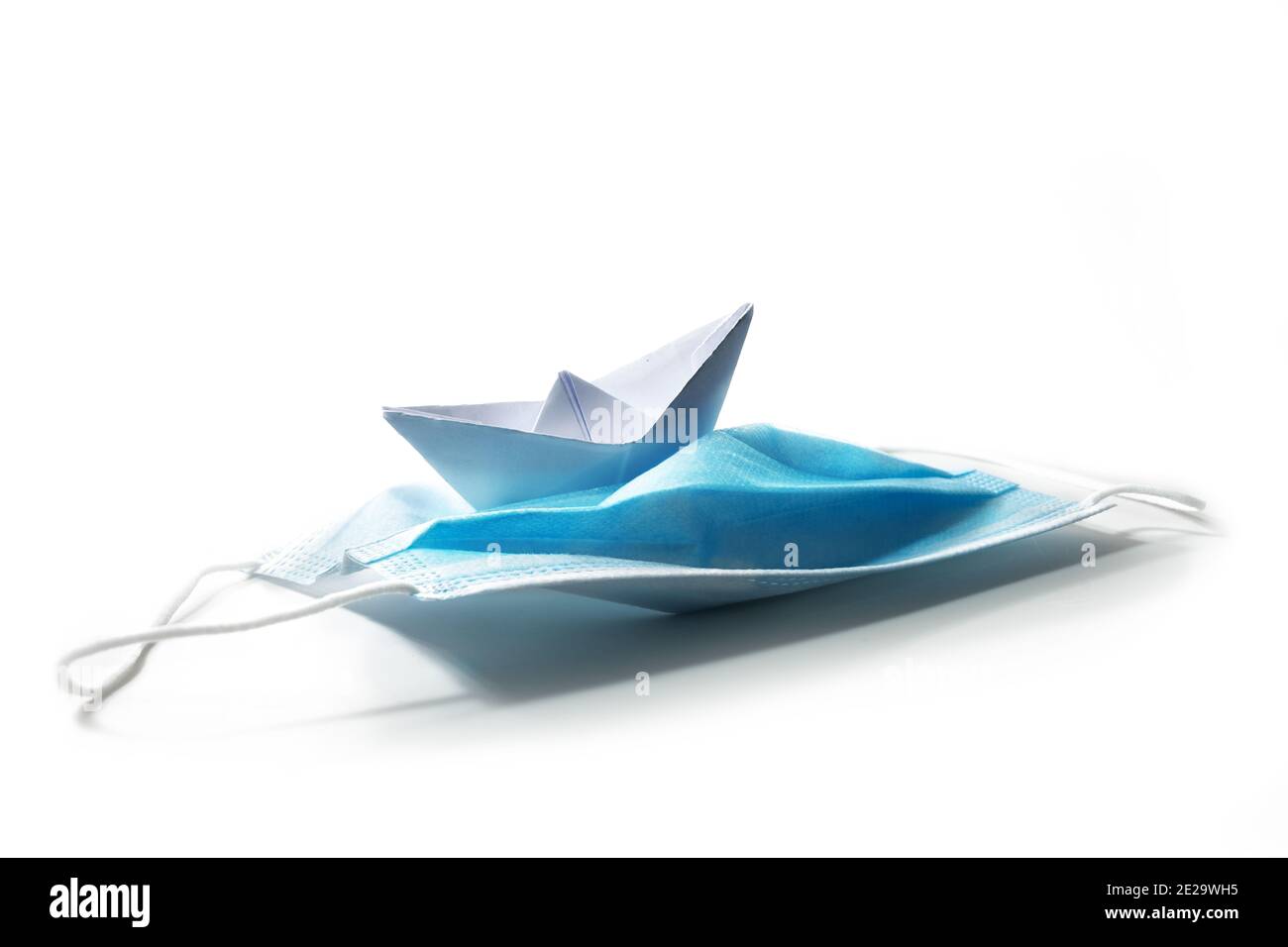 Papierboot Kurs halten auf einer chirurgischen Gesichtsmaske gegen covid-19 Pandemie als Schiff Reiten in stürmischen Meeren, Coronavirus Krise Konzept, isoliert auf w Stockfoto
