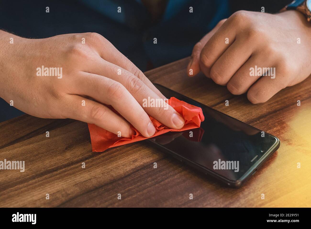 Die Hände des Mannes wischen den Handybildschirm mit einer Serviette aus nächster Nähe ab. Stockfoto