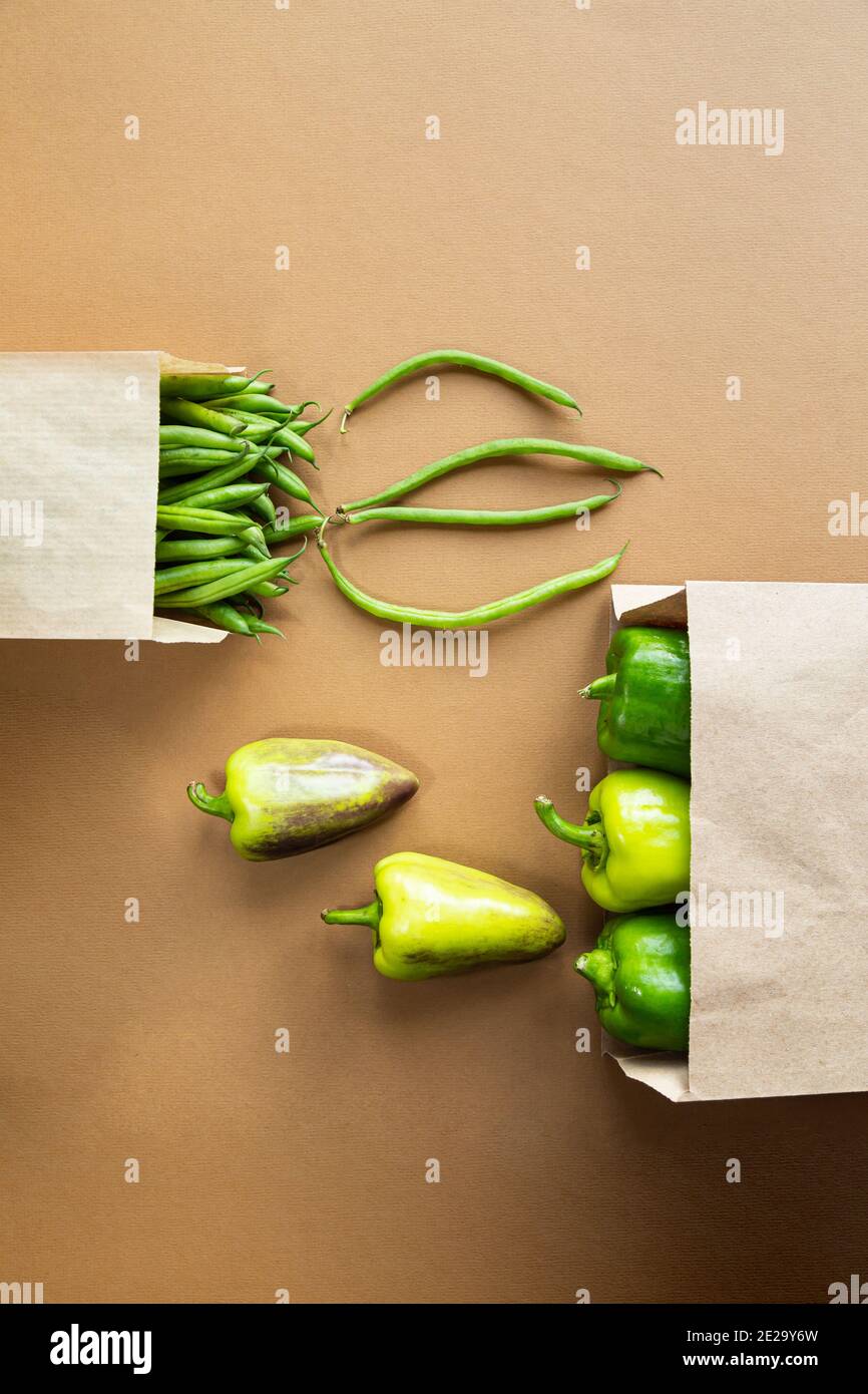 Grüne Bohnen und Paprika in einem Bastelpapierbeutel auf braunem Hintergrund. Ernten Sie gesunde Bio-Lebensmittel Stockfoto