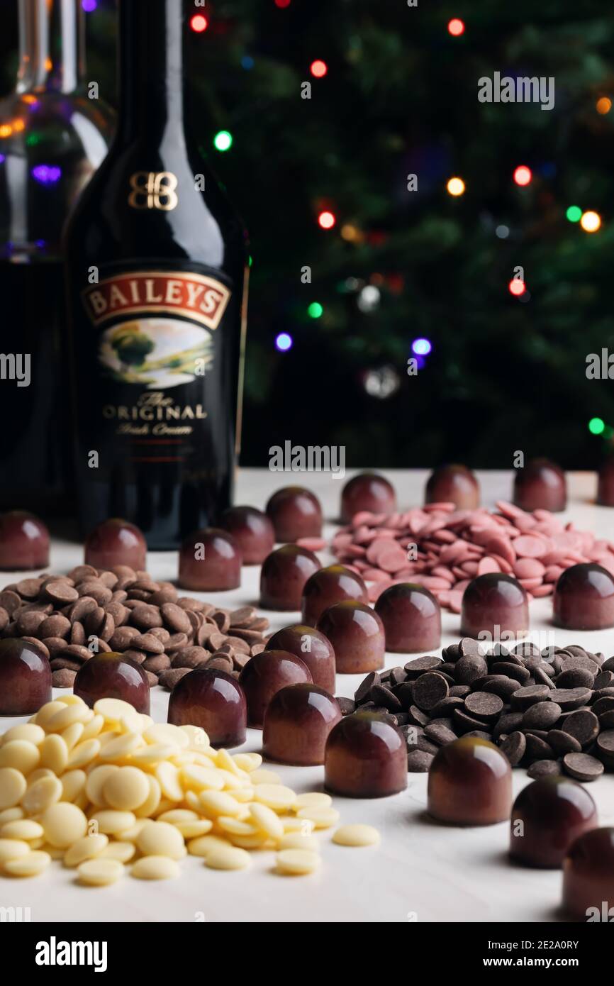 Verschiedene dunkle, milchige, weiße und farbige Schokolade in Kalbskörtchen und Flaschen mit Cremelikör auf dem Hintergrund der Weihnachtsbeleuchtung Stockfoto