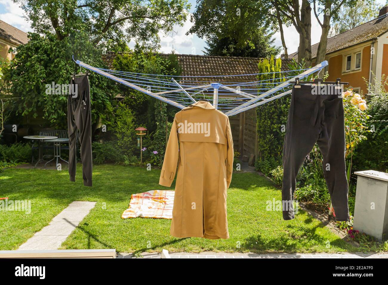 Wintermantel und Jogginghose hängen bei sonnigem Wetter an der Wäscheleine im Hinterhof. Weitwinkel. Stockfoto