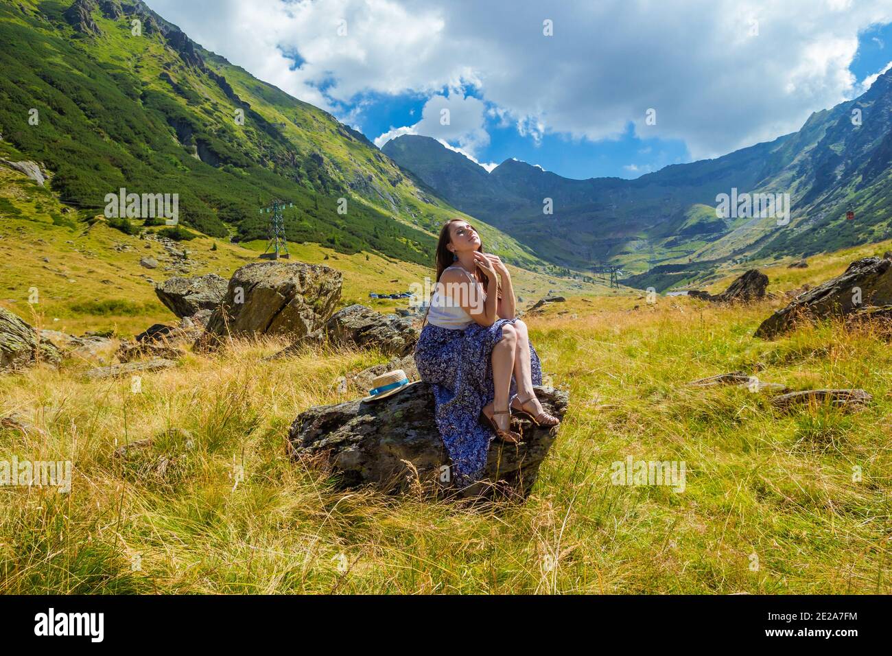 Mädchen in langen blauen Kleid sitzt auf einem Felsen in Die Berge Stockfoto