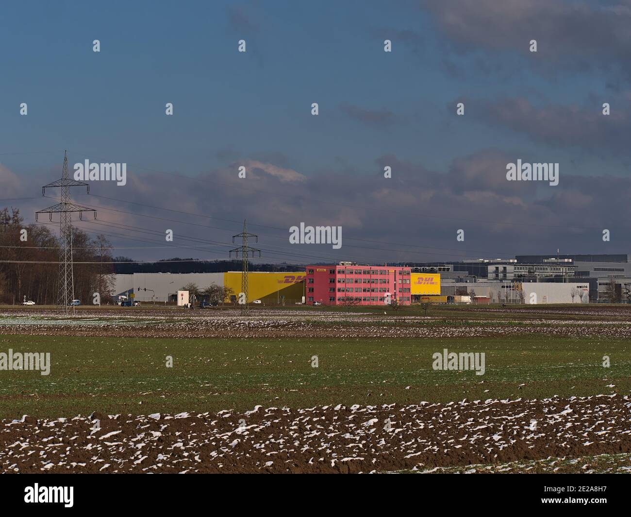 Logistikzentrum des Transportunternehmens DHL Global Forwarding, Teil der Deutsche Post DHL Group, mit Firmenlogo und landwirtschaftlichen Feldern. Stockfoto