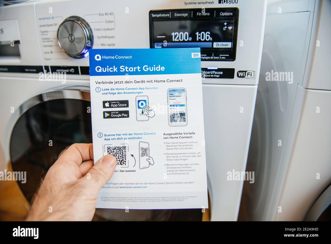 Paris, Frankreich - Jan 5, 2020: POV männliche Hand hält Bosch Home Connect Kurzanleitung mit zwei neuesten Siemens Wasch- und Trocknungsmaschine im Hintergrund Stockfoto