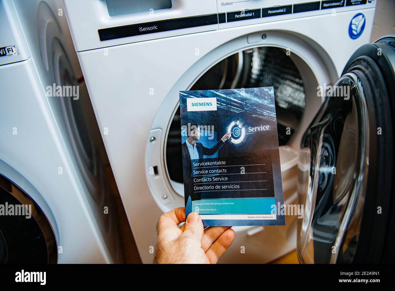 Paris, Frankreich - 5. Jan 2020: POV männliche Hand hält Bosch Service Kontakt Flyer Werbeinformatio Guide mit zwei neuesten Siemens Wasch- und Trocknungsmaschinen im Hintergrund Stockfoto
