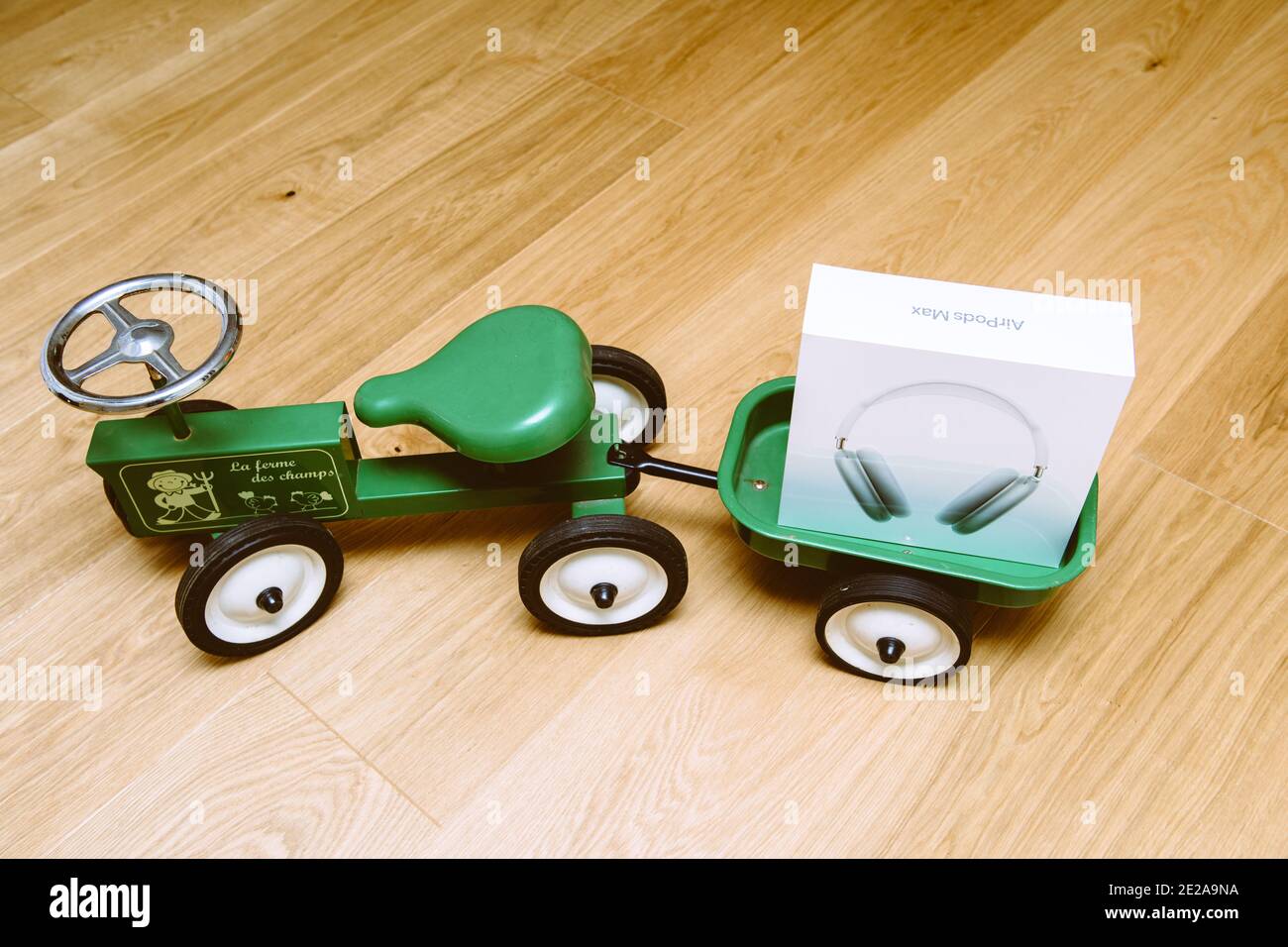 Paris, Frankreich - Jan 7, 2020: Ansicht von oben von Kid Kind grünen Traktor Spielzeug mit Apple Computers AirPods Max über-Ohr-Kopfhörer im Kofferraum Stockfoto