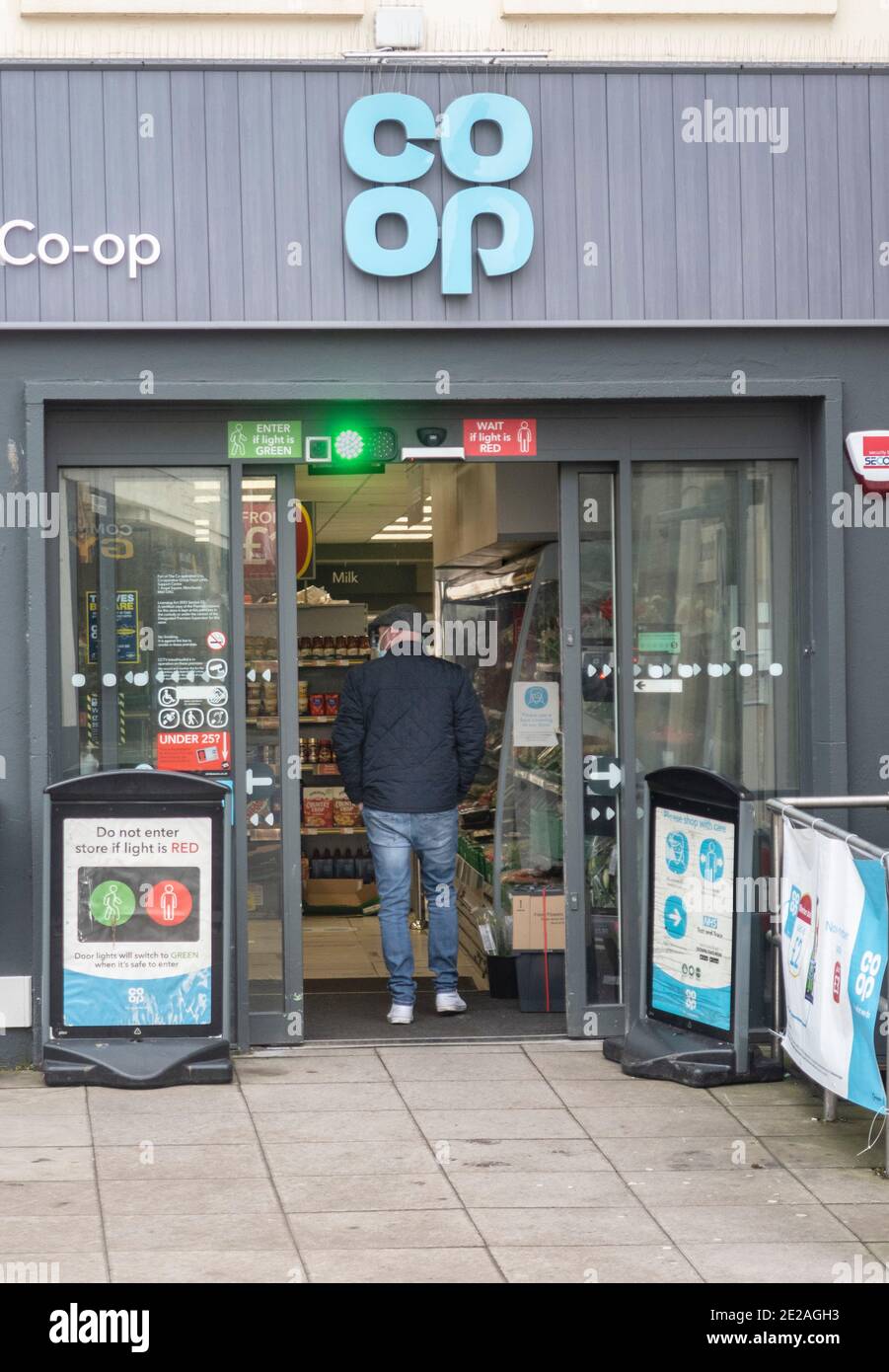 Ein Mann betritt über eine Ampelanlage, Co op Supermarkt speichern während Covid Coronavirus Einschränkungen in Sidmouth Devon UK Stockfoto