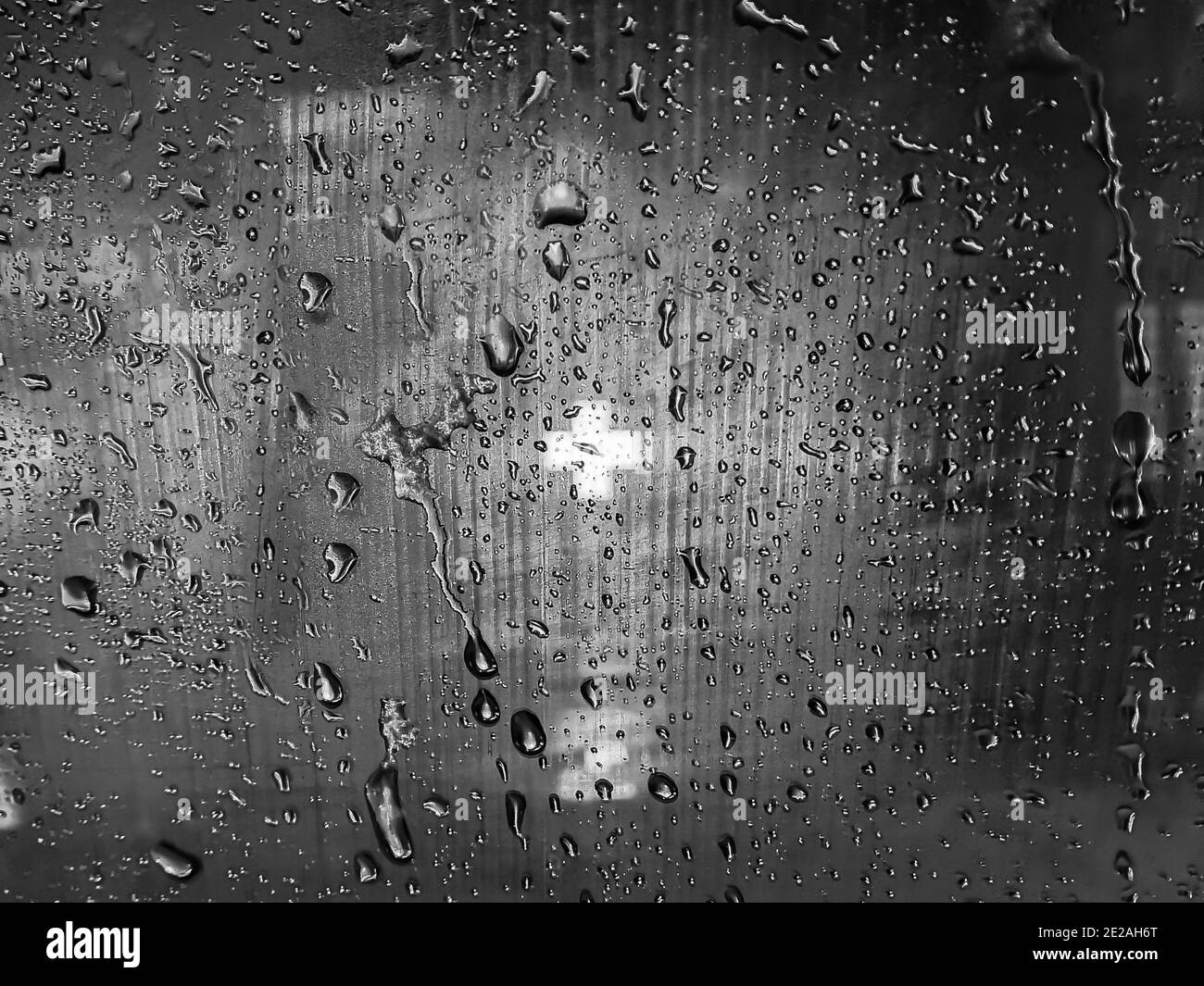 Der Anblick eines medizinischen Kreuzes, das in der Dunkelheit an der Apotheke durch das vernebelte Glas glüht, als letzte Hoffnung auf Rettung. Schwarz-weißes Glas Stockfoto