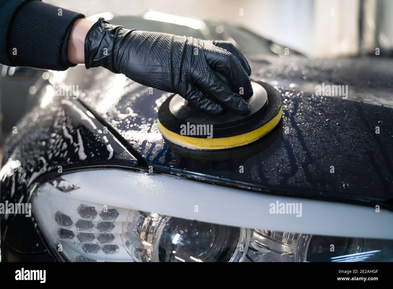 Mann reinigt Autohaube mit Kreis Schwamm. Automatische Vorbereitung für das Polieren. Detaillierte Autowäsche Stockfoto