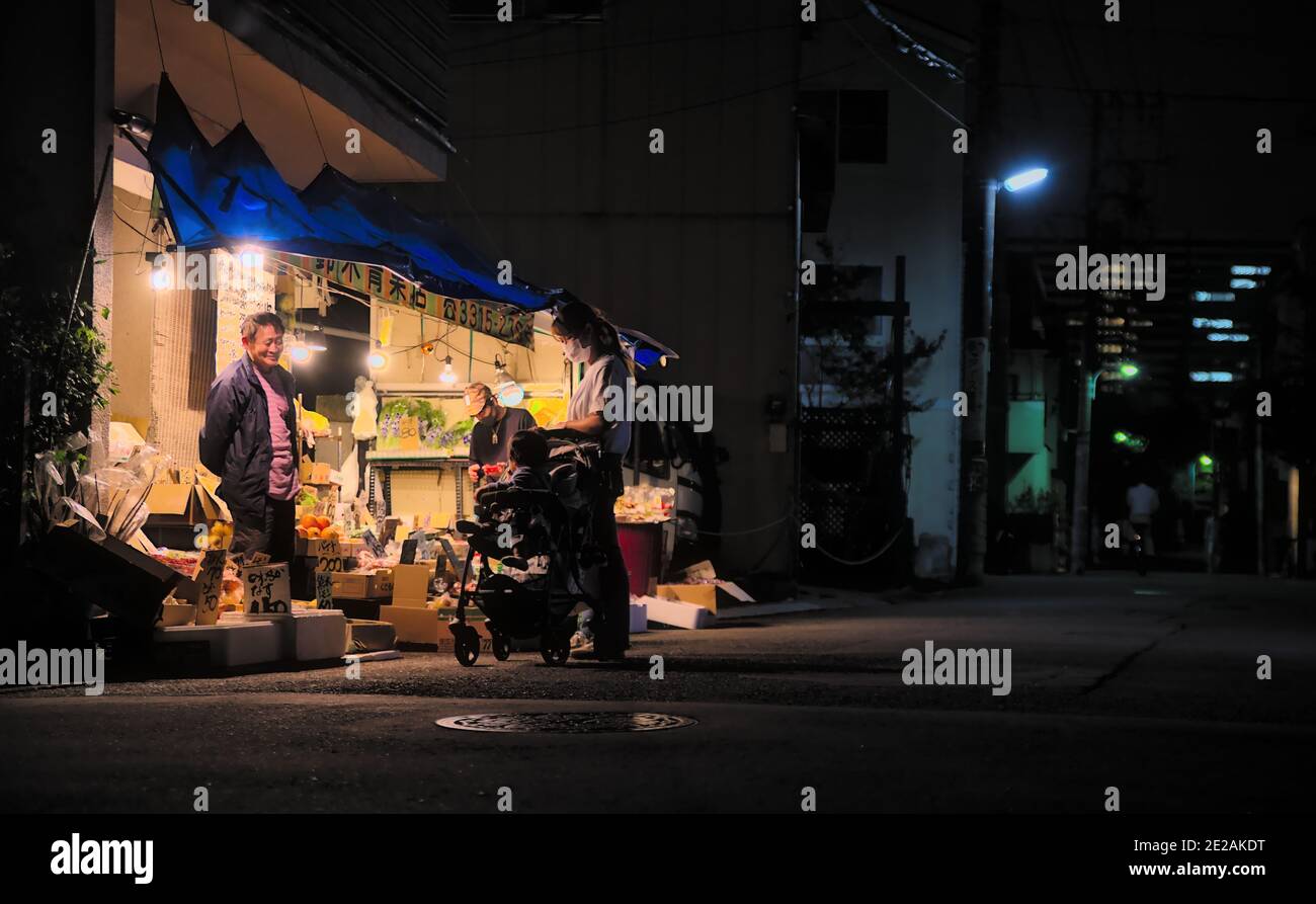 Nachtansicht eines Paares mit einem Kleinkind in einem Kinderwagen, der in einem kleinen Laden in einem westlichen Vorort von Tokio shoppt Stockfoto