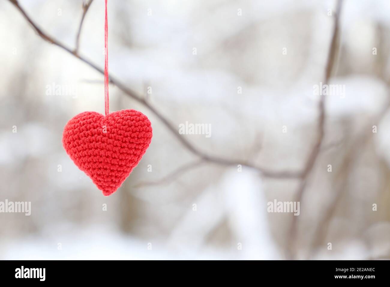 Valentine Herz im Winterwald. Rot gestricktes Symbol der Liebe hängt auf einem Zweig, Hintergrund für den Urlaub Stockfoto