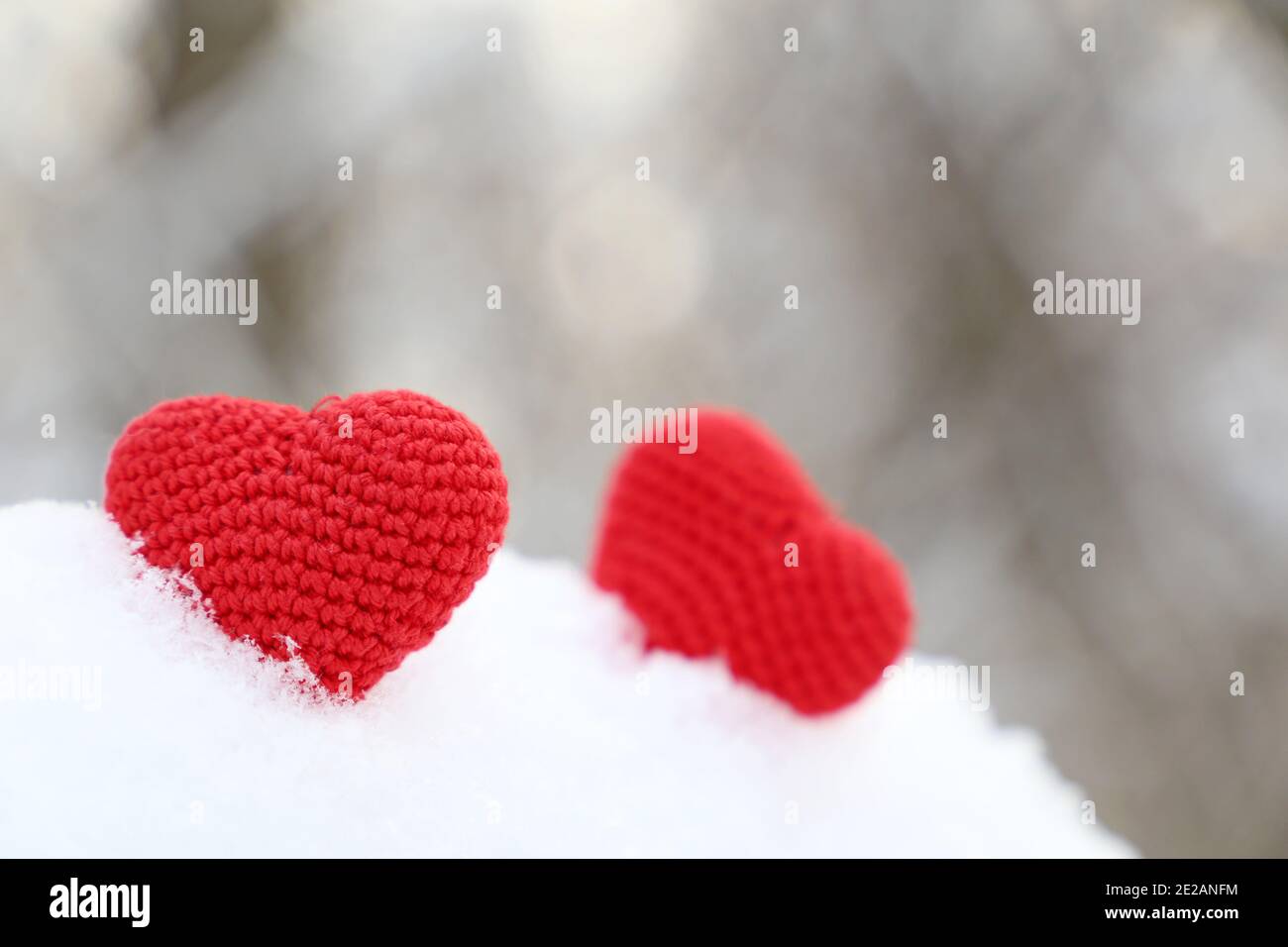 Valentine Herzen im Winterwald im Sonnenlicht. Zwei rote gestrickte Herzen auf Schnee, Symbol der romantischen Liebe, Hintergrund für den Urlaub Stockfoto