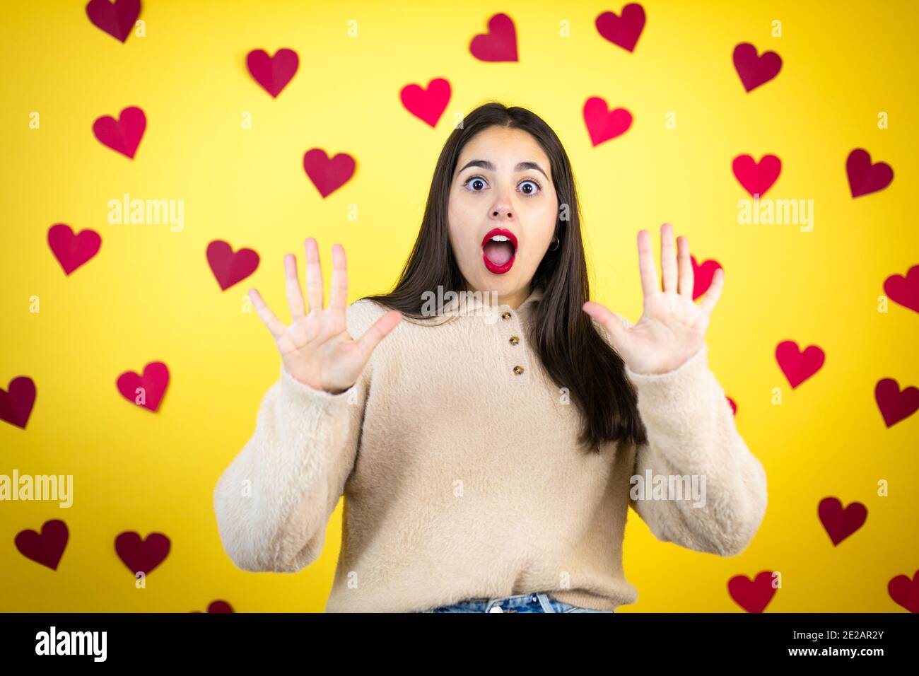 Junge kaukasische Frau auf gelbem Hintergrund mit roten Herzen Angst und erschrocken vor Angst Ausdruck Stop Geste mit Händen, schreien im Schock. Schwenken Stockfoto