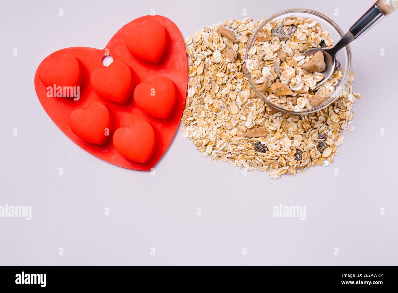 Müsli und Silikonform in Form eines roten Herzens auf ultimativ grauem Hintergrund. Stockfoto