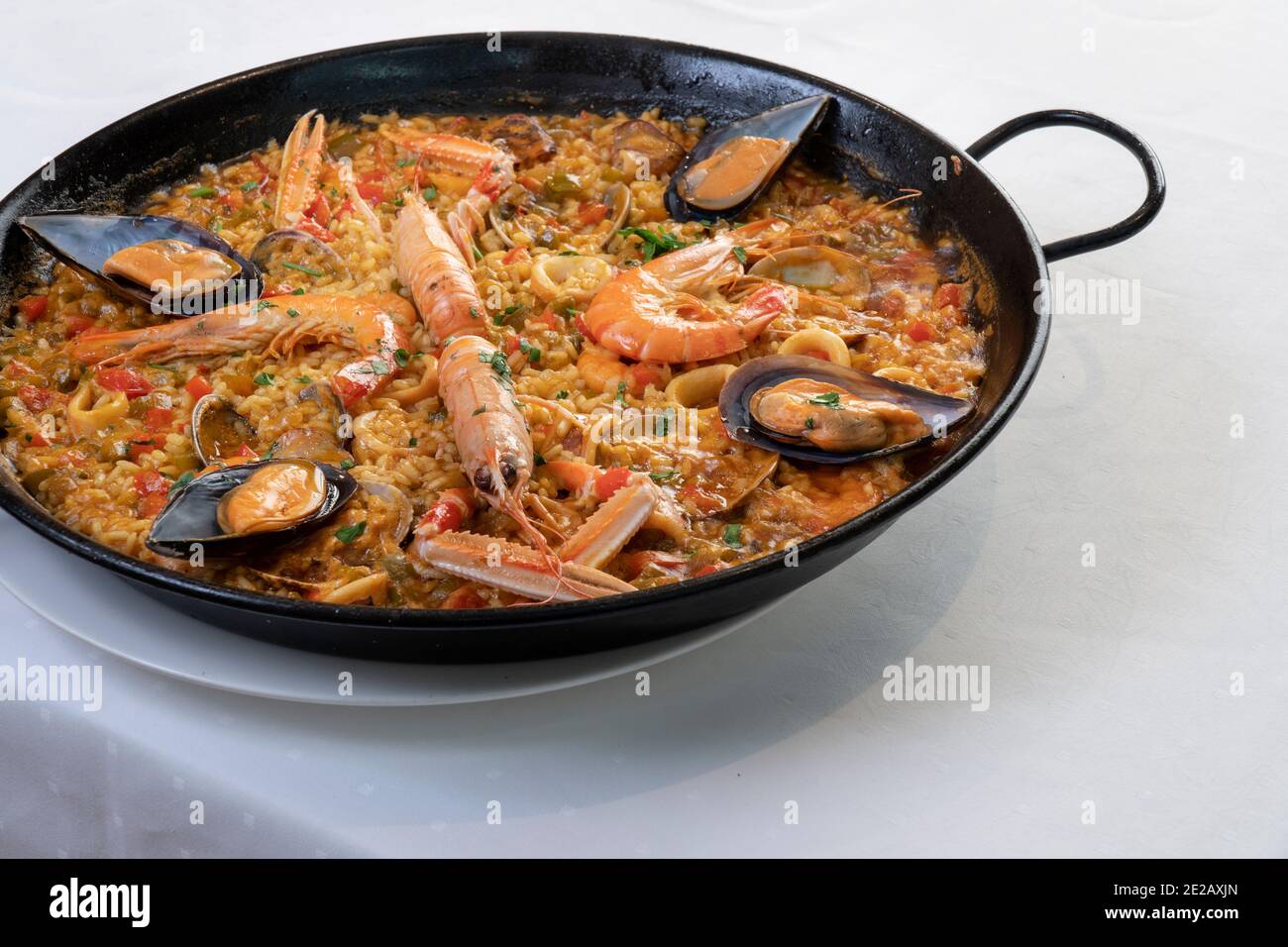 Spanische Paella mit Meeresfrüchten, mit Krebsen, Tintenfisch, Muscheln und Garnelen, in einer eisernen Pfanne auf weißem Hintergrund Stockfoto