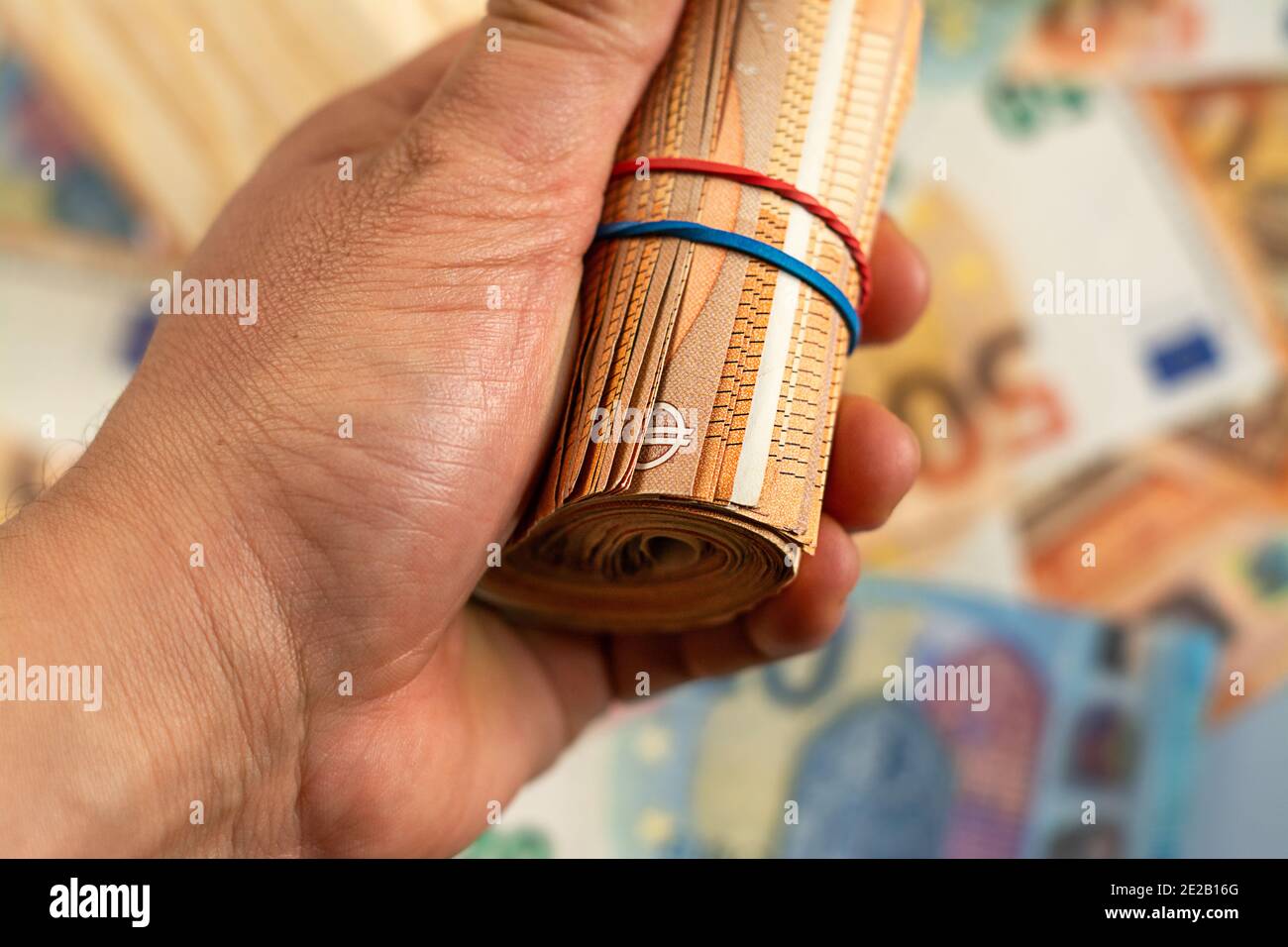 Nahaufnahme der Hand, die eine Rolle von Euro-Geldrechnung auf einem Geldhintergrund hält, Euro-Geld der Europäischen Union Stockfoto