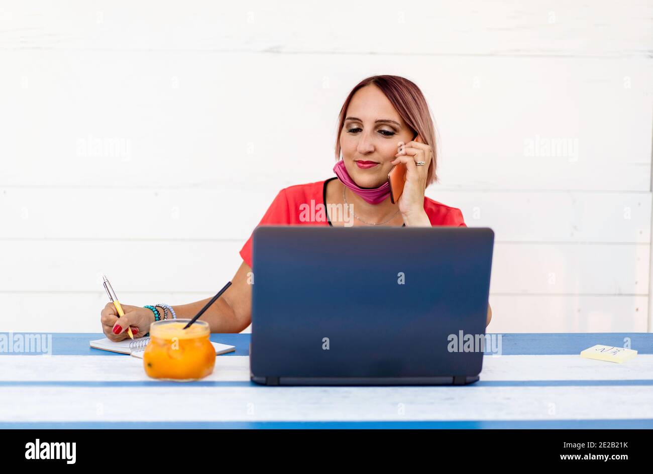 Lächelnde Frau 40 Jahre alt trägt offene Schutzmaske mit Laptop und Handy während des Endes des Coronavirus Ausbruch. Unternehmerin w Stockfoto