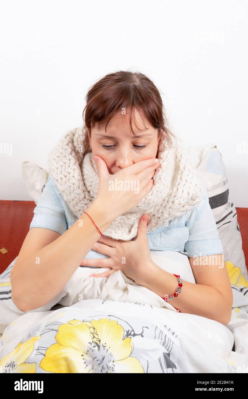 Ein junges hübsches Mädchen ist zu Hause krank, liegt im Bett, hustet und hält sich an ihre Brust und bedeckt ihren Mund mit der Hand Stockfoto