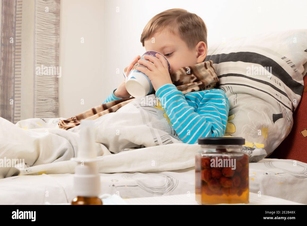 Krankes Kind Junge in einem blauen Pullover in einem eingewickelt Warme Schal im Bett trinken Ingwertee mit Honig Stockfoto