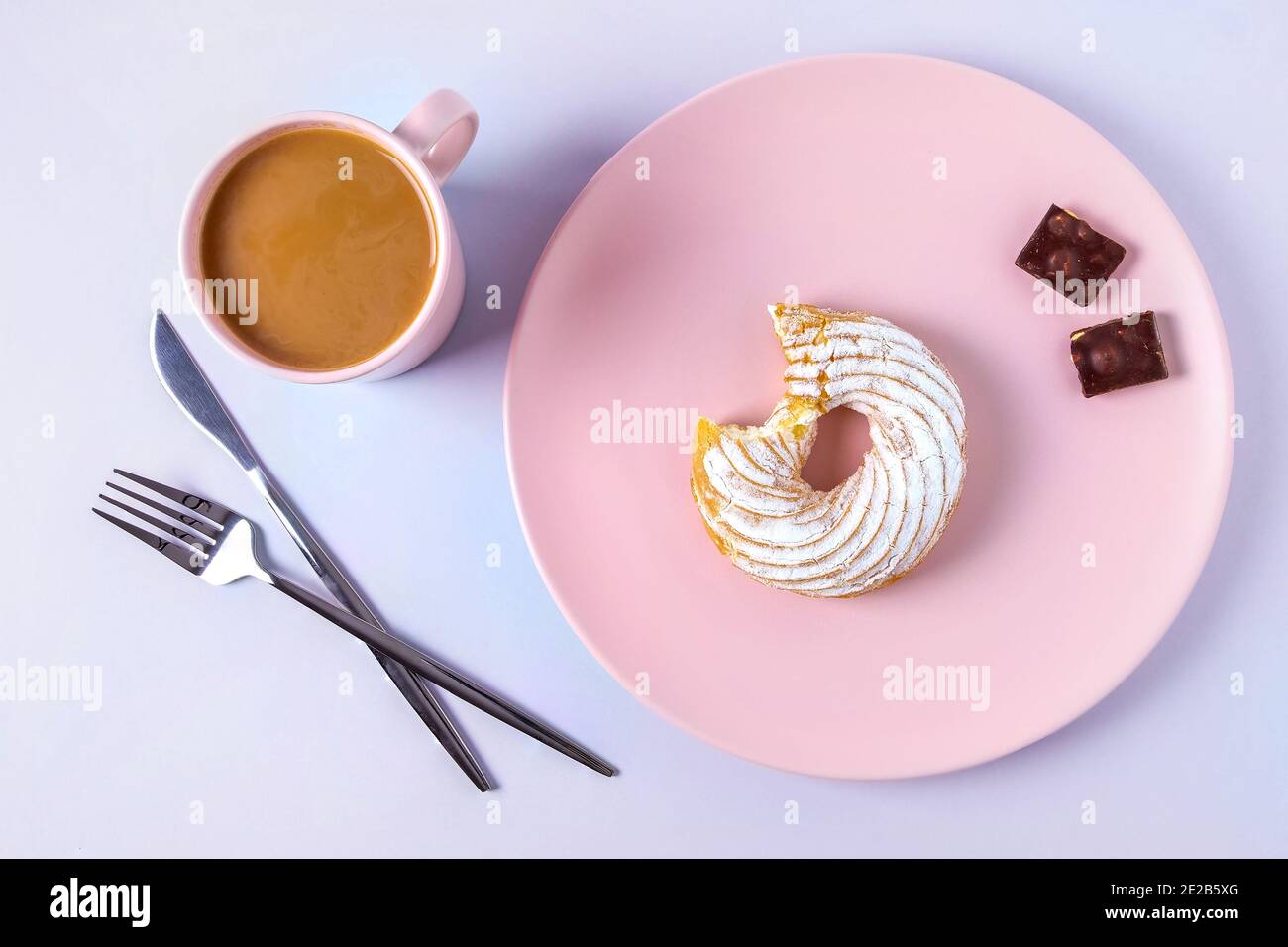 Draufsicht auf Stillleben eines gebissenen Kuchens auf einem rosafarbenen Teller, Besteck und einer Tasse Kakao oder Kaffee mit Milch. Selektiver Fokus, horizontale Ausrichtung. Stockfoto